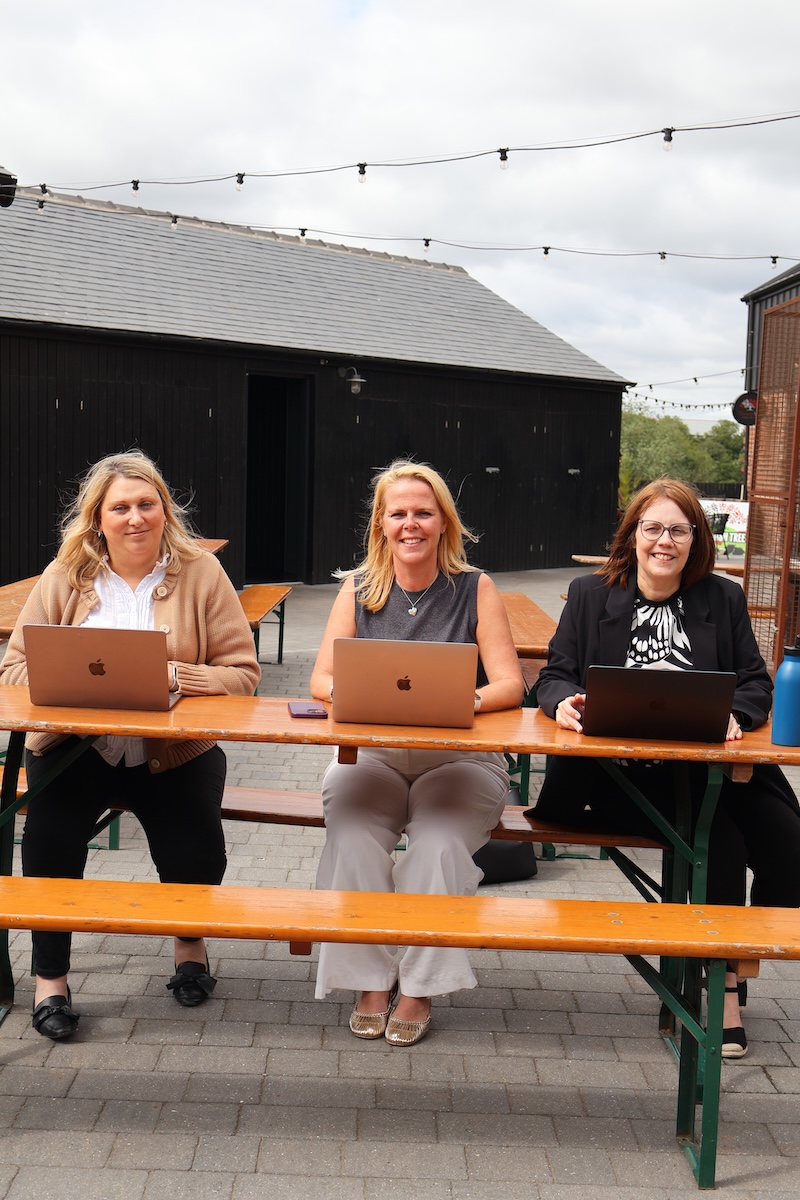 3 HR consultants sitting at a bench with open macbooks.